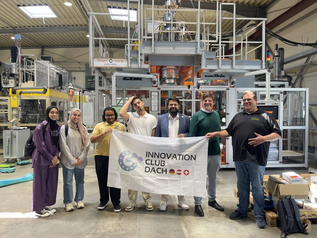 Innovation Club DACH mit Club-Fahne in einer Produktionshalle